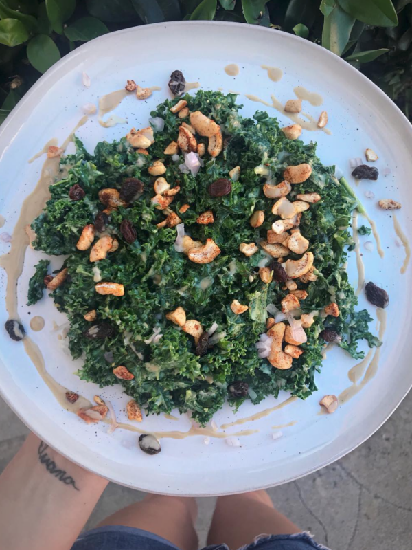 kale salad with tahini sauce and cashews on a white plate