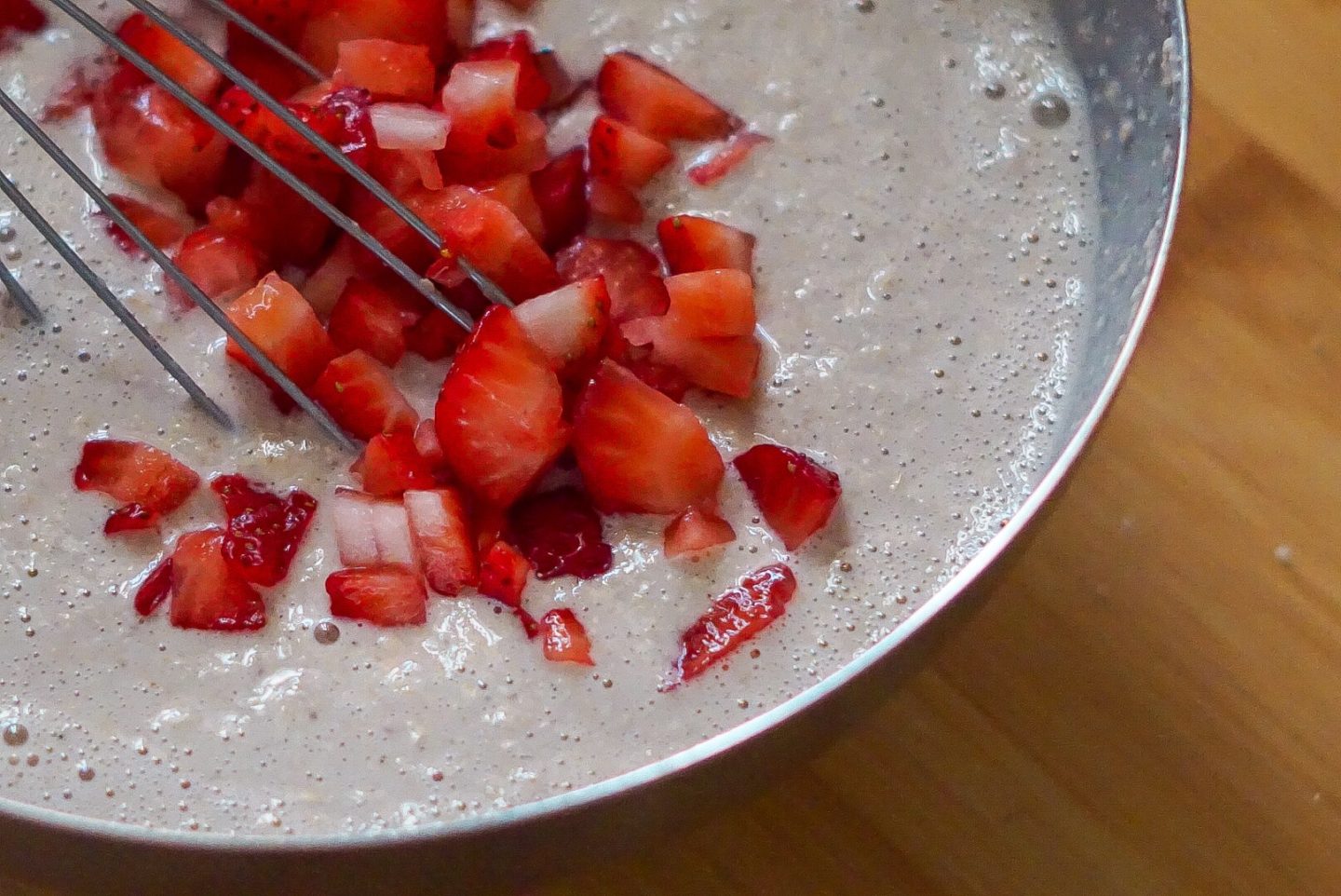 muffin batter in a mixing bowl with fresh strawberries