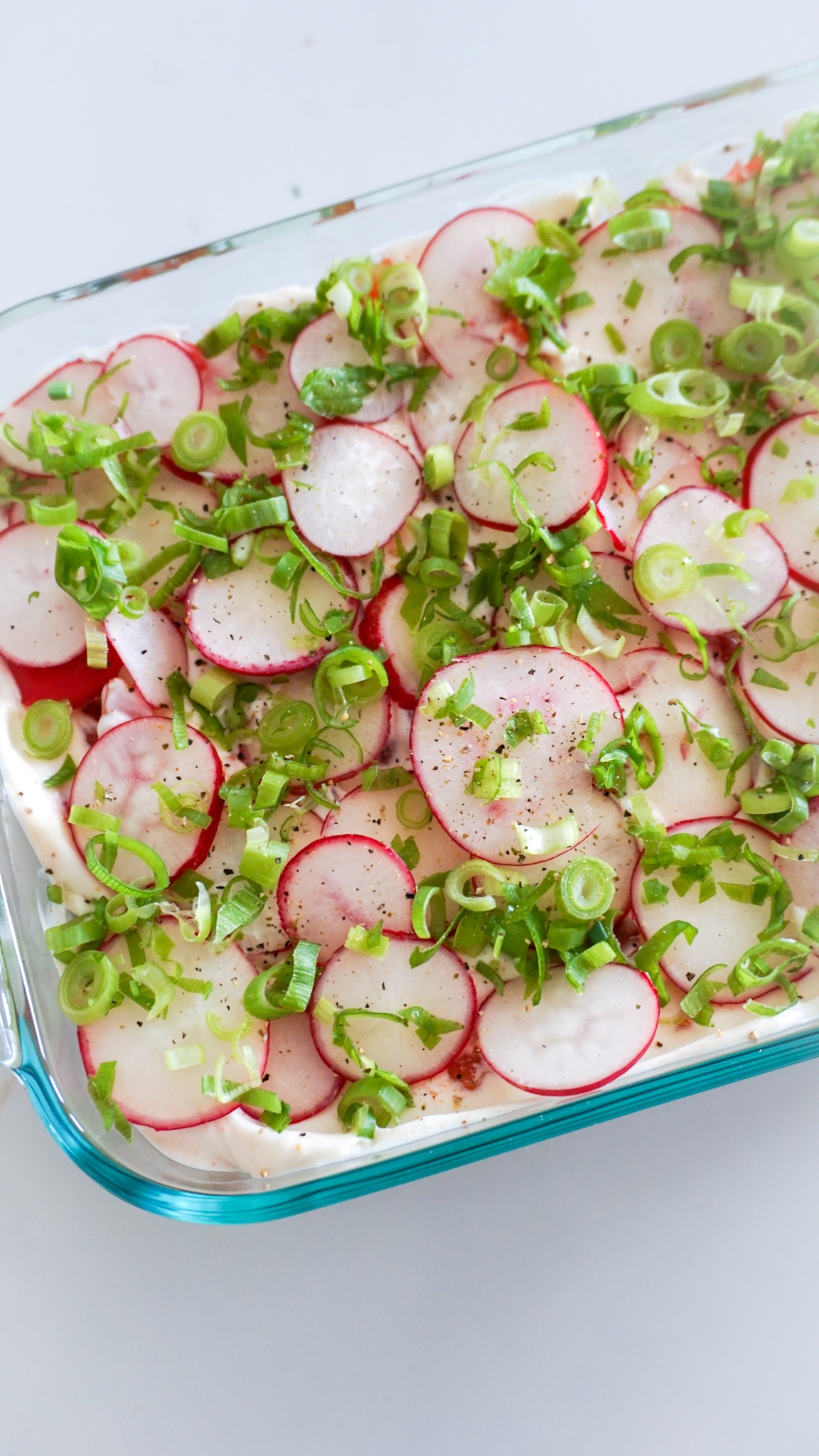 seven layer dip appetizer with radishes and scallions in a glass dish