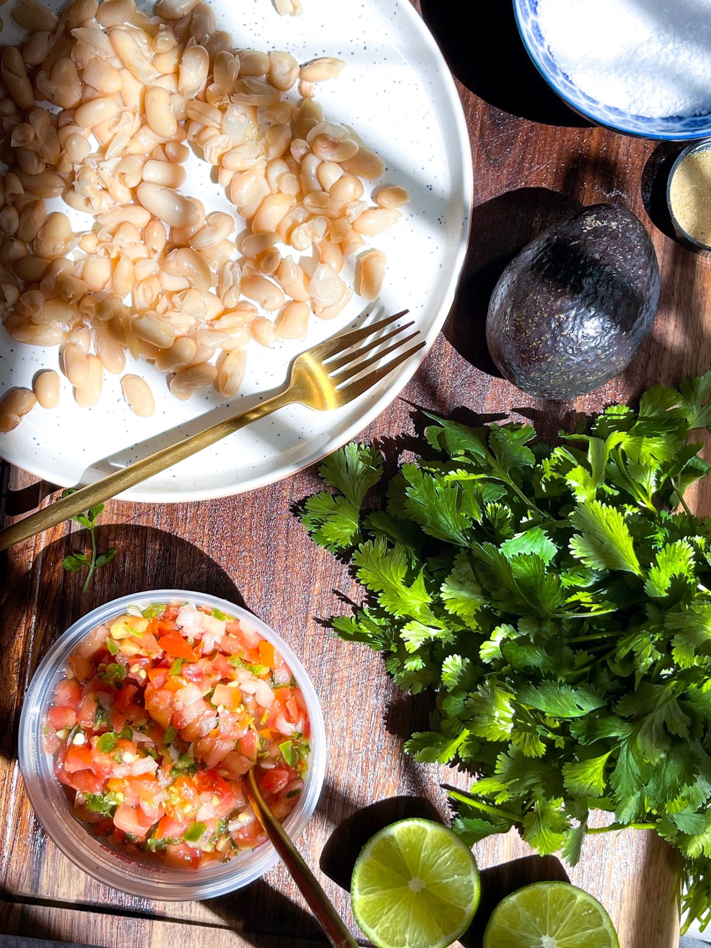 salsa, cilantro, white beans and an avocado on a wooden cutting board