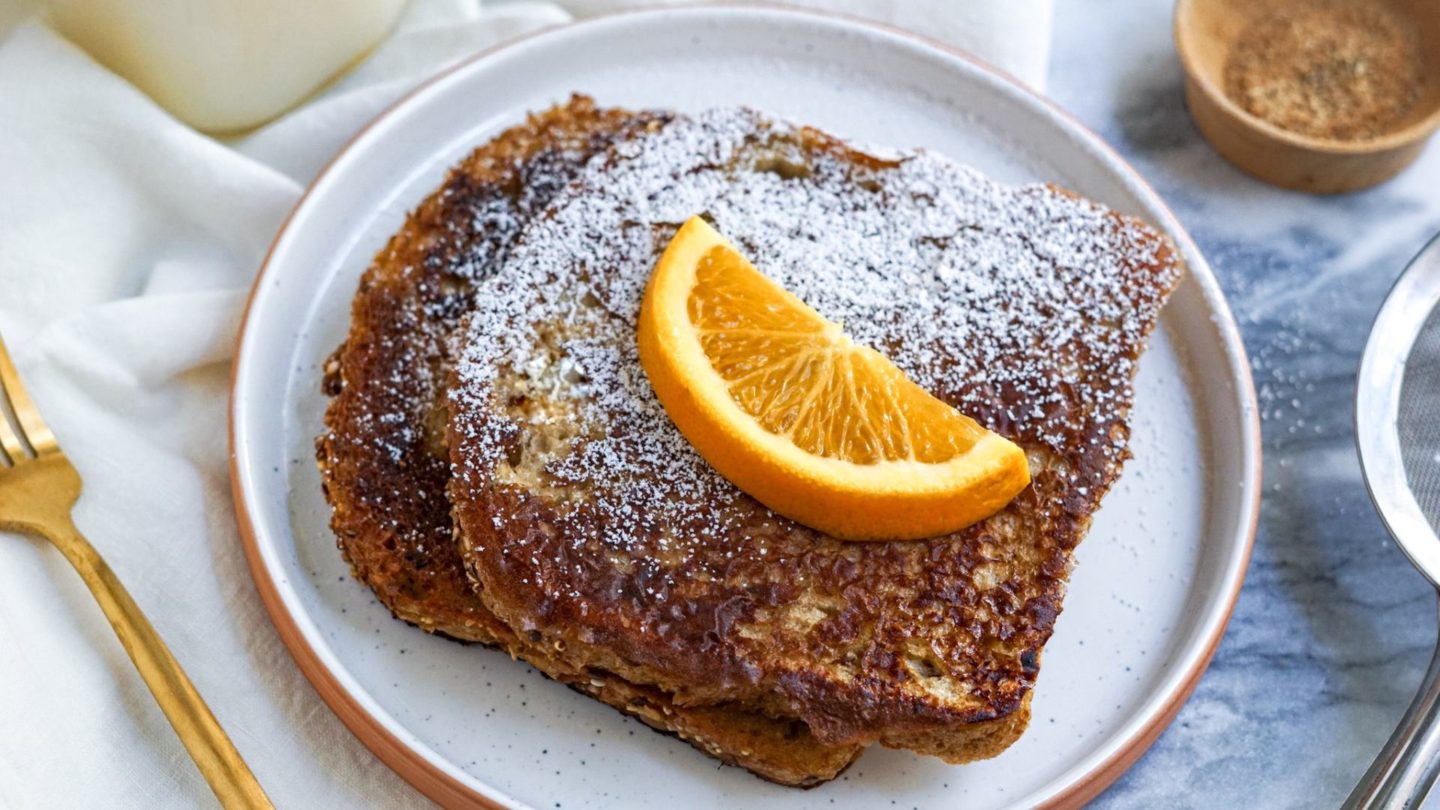 vegan French toast with oranges and powdered sugar on a white plate