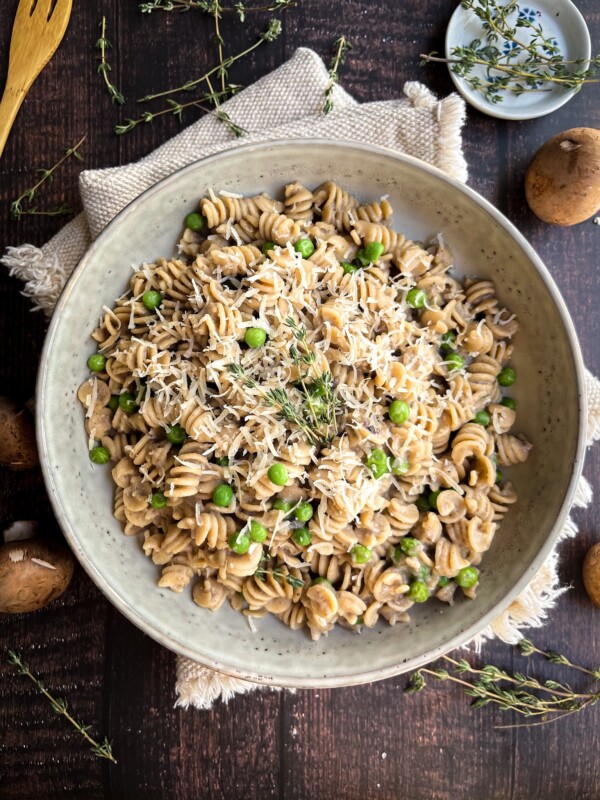 mushroom pasta with peas in a cream colored bowl