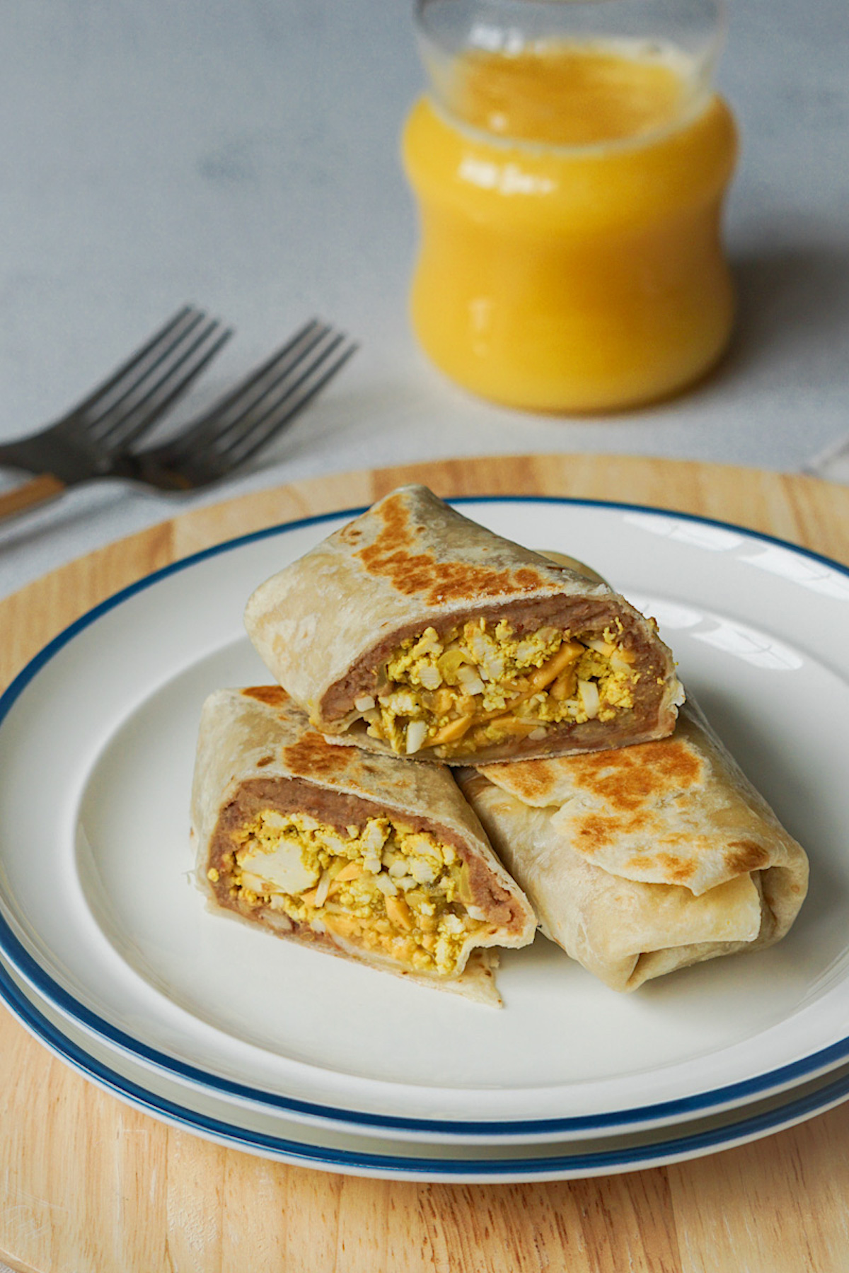 vegan breakfast burritos sliced in half on a white plate next to a glass of orange juice for breakfast 